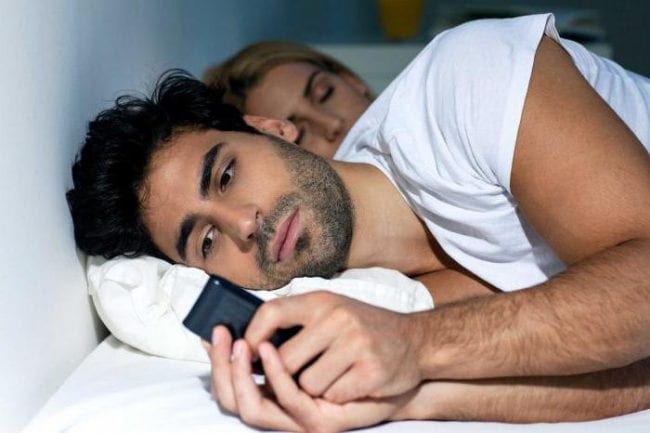 Мужчина с телефоном и спящая жена