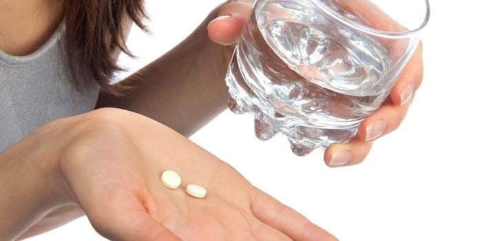 Девушка держит таблетки и стакан воды