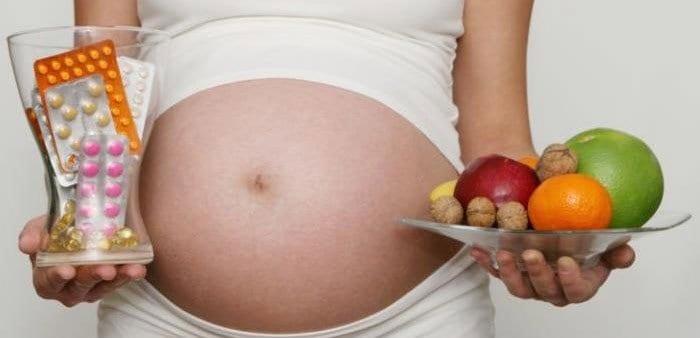 Беременная женщина с таблетками и фруктами в руках