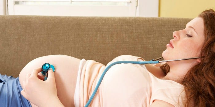 Беременная женщина лежит на диване и слушает свой живот