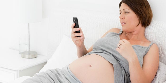 Беременная девушка с телефоном лежит в кровати