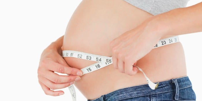 Беременная женщина измеряет живот сантиметром