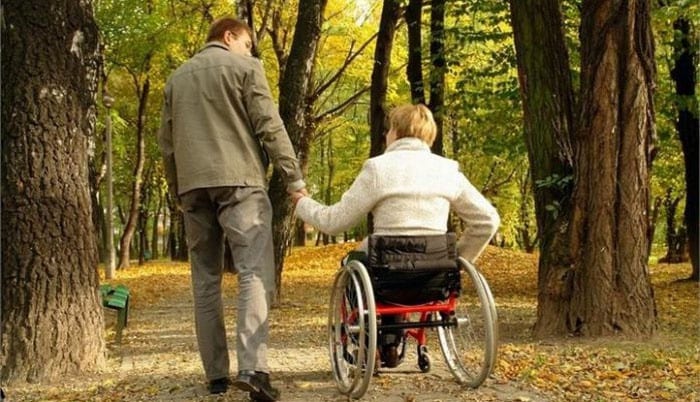 Мужчина держит за руку женщину в инвалидной коляске