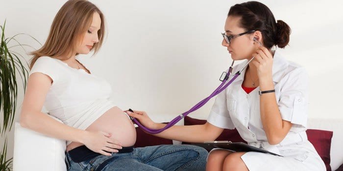 Медик слушает сердцебиение ребенка в животе беременной девушки